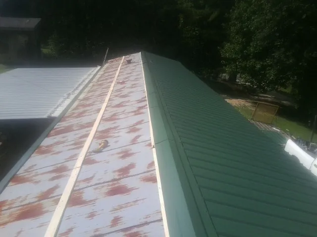 Old rusted panels beside newly installed green metal roofing — Wind Damage Roof Repair by Roofing Brothers in Felton