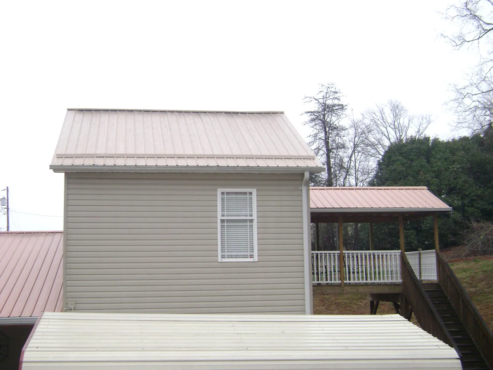 Tan metal roofs on a two story addition and attached porch, from a Roof Replacement job in Felton
